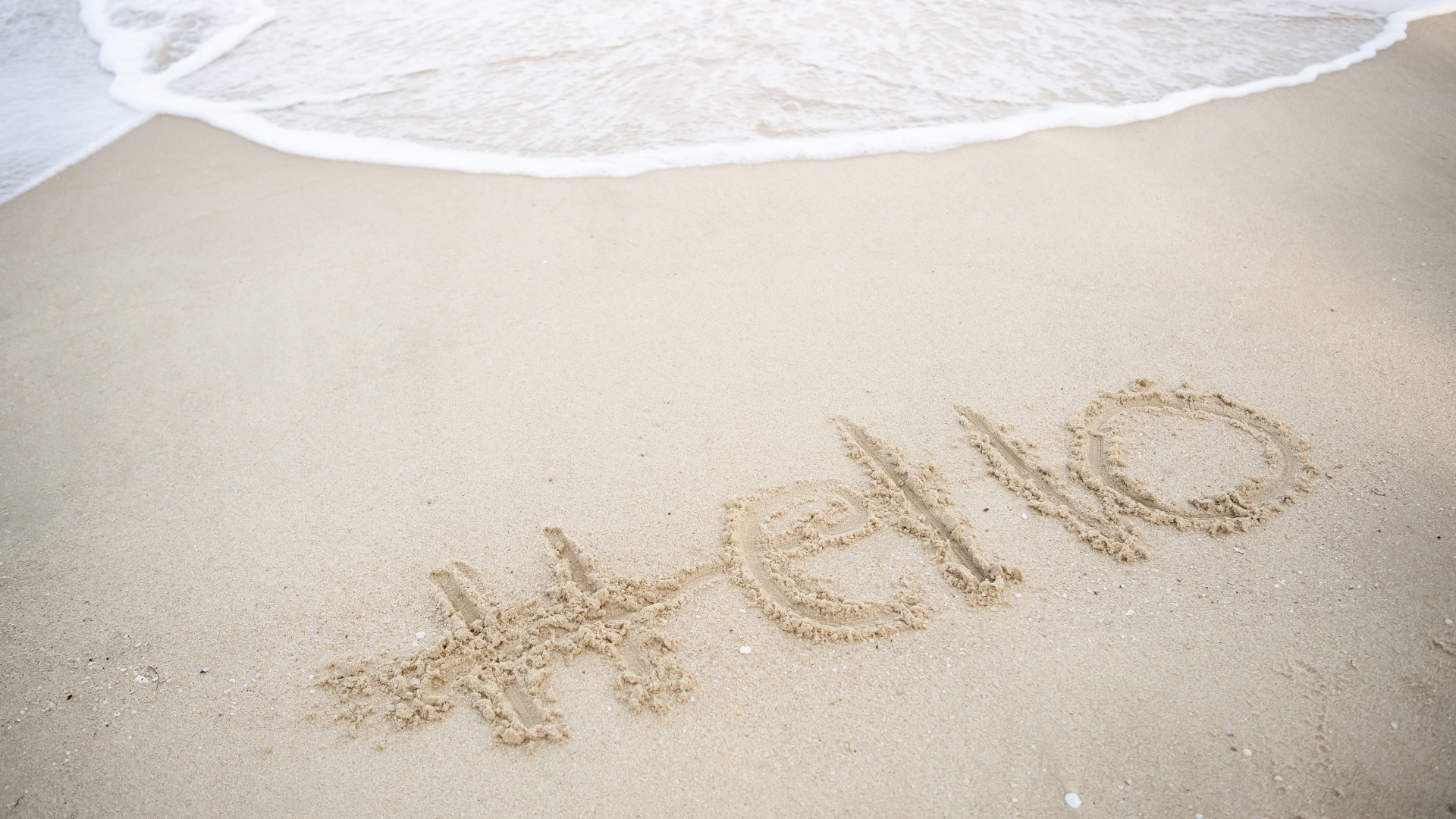 Надпись Hello на мокром песке у моря летом 