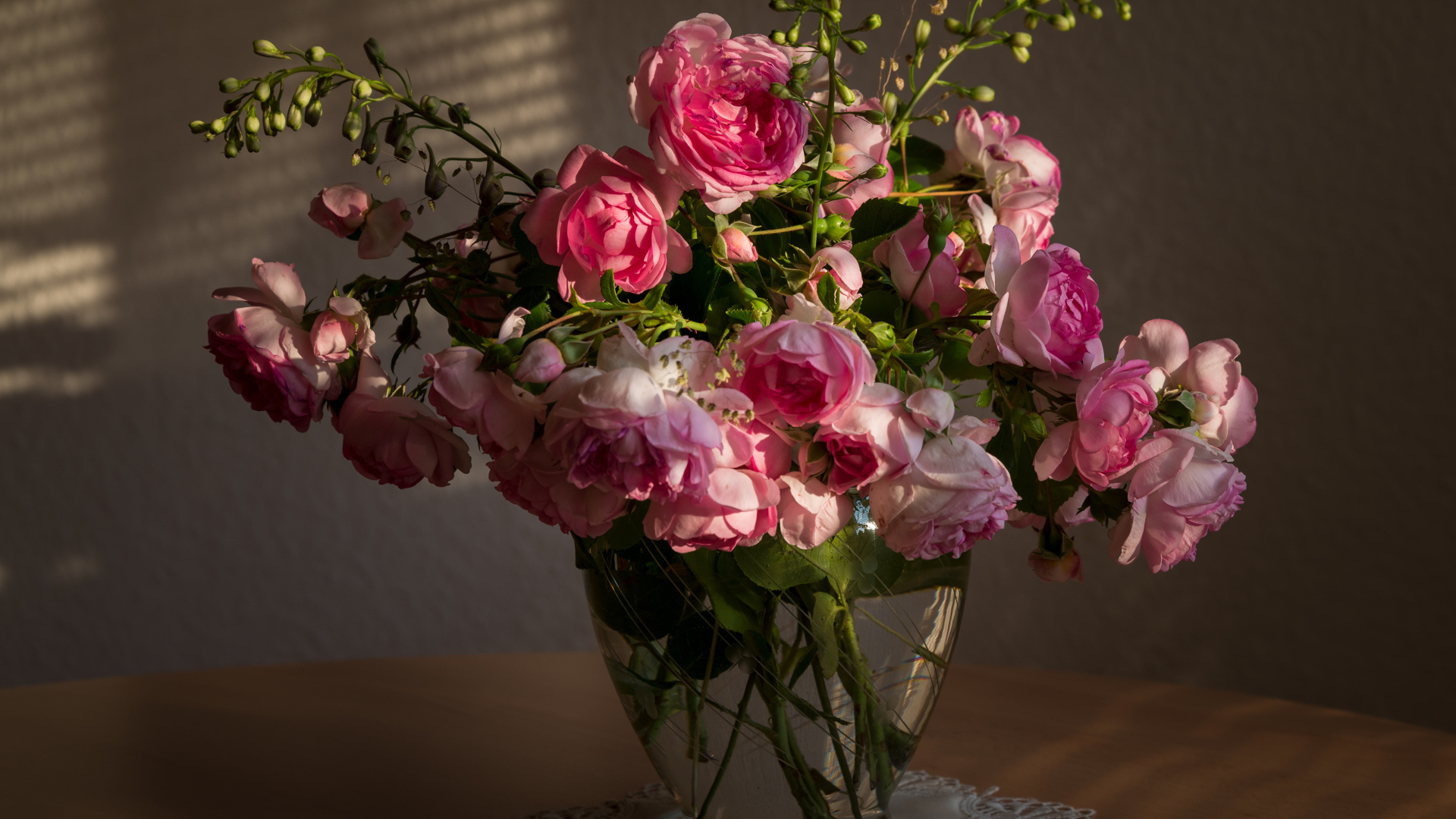 Букет розовых роз в стеклянной вазе не столе в лучах солнца 