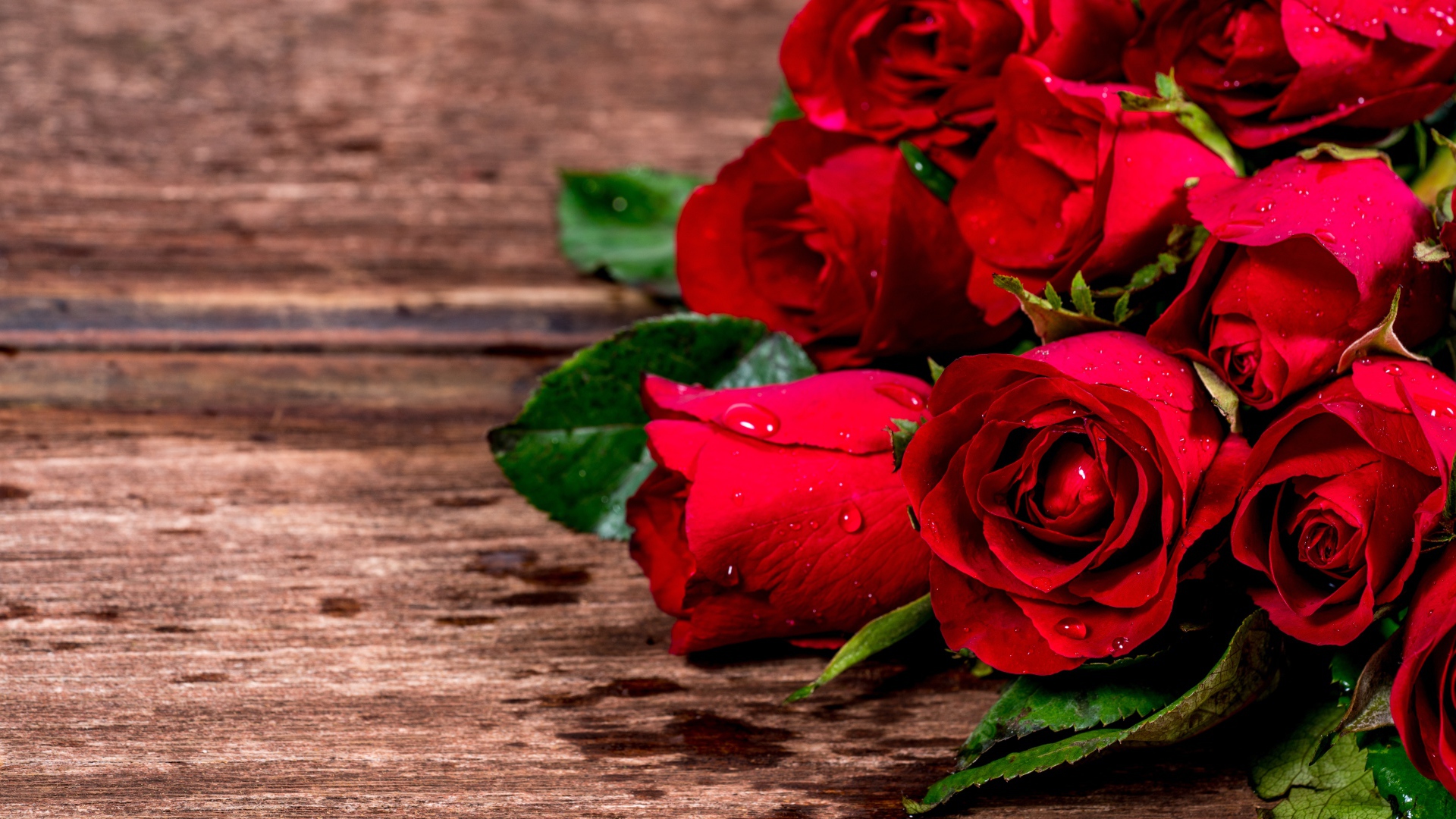 Букет красных роз на деревянном столе в каплях воды