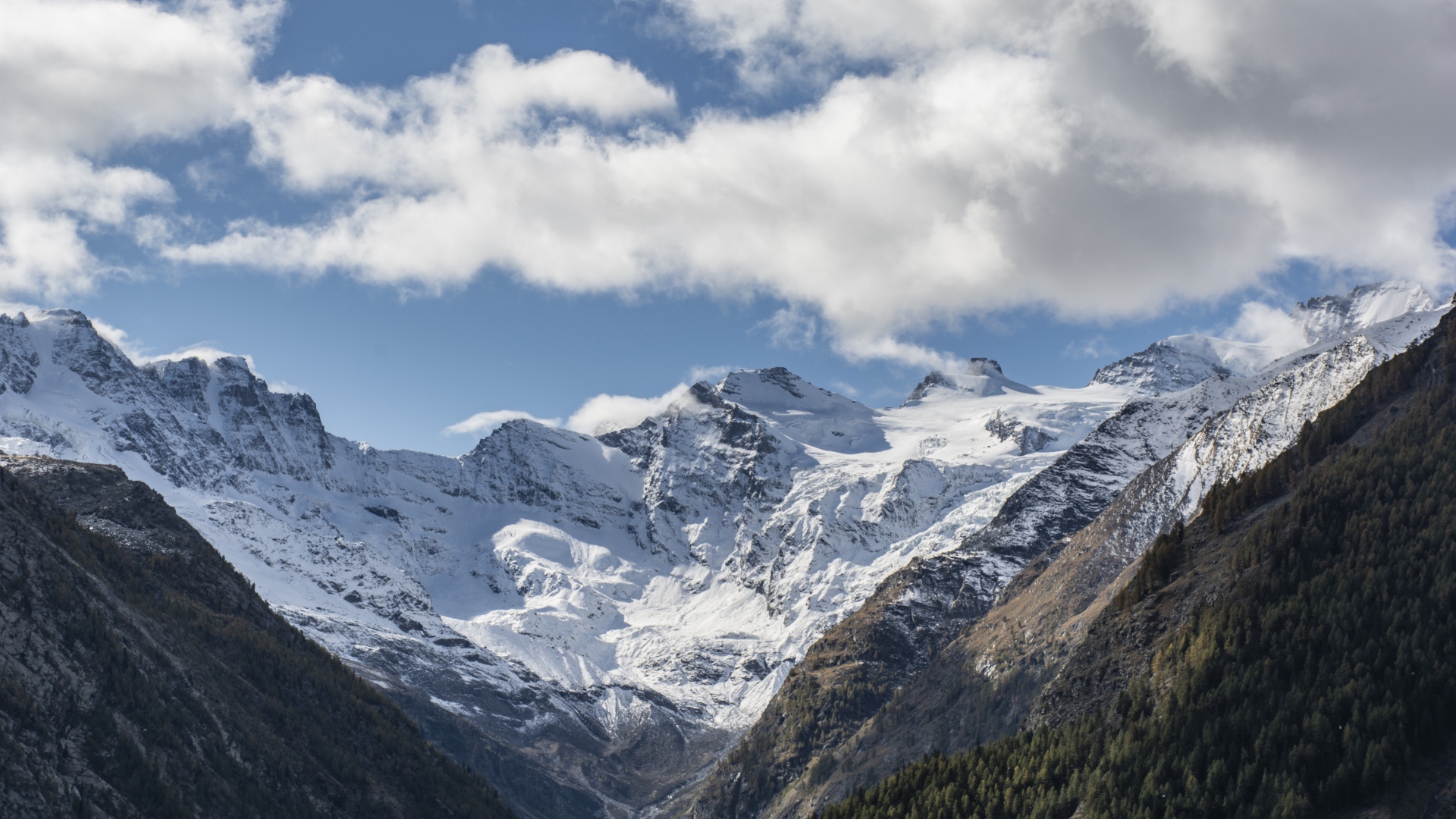 Заснеженные горы под голубым небом с белыми облаками
