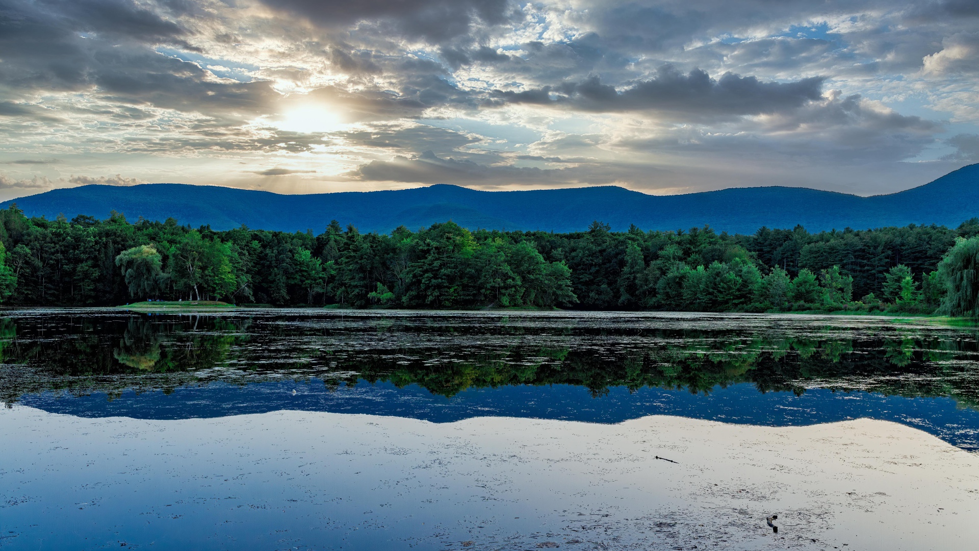 Солнце пробивается сквозь облака в небе над озером