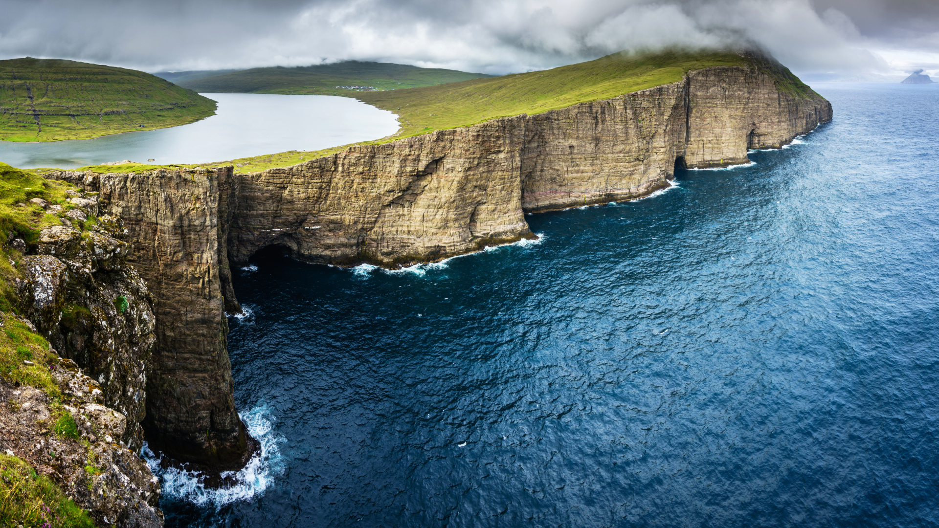 Океан омывает зеленый утес под пасмурным небом