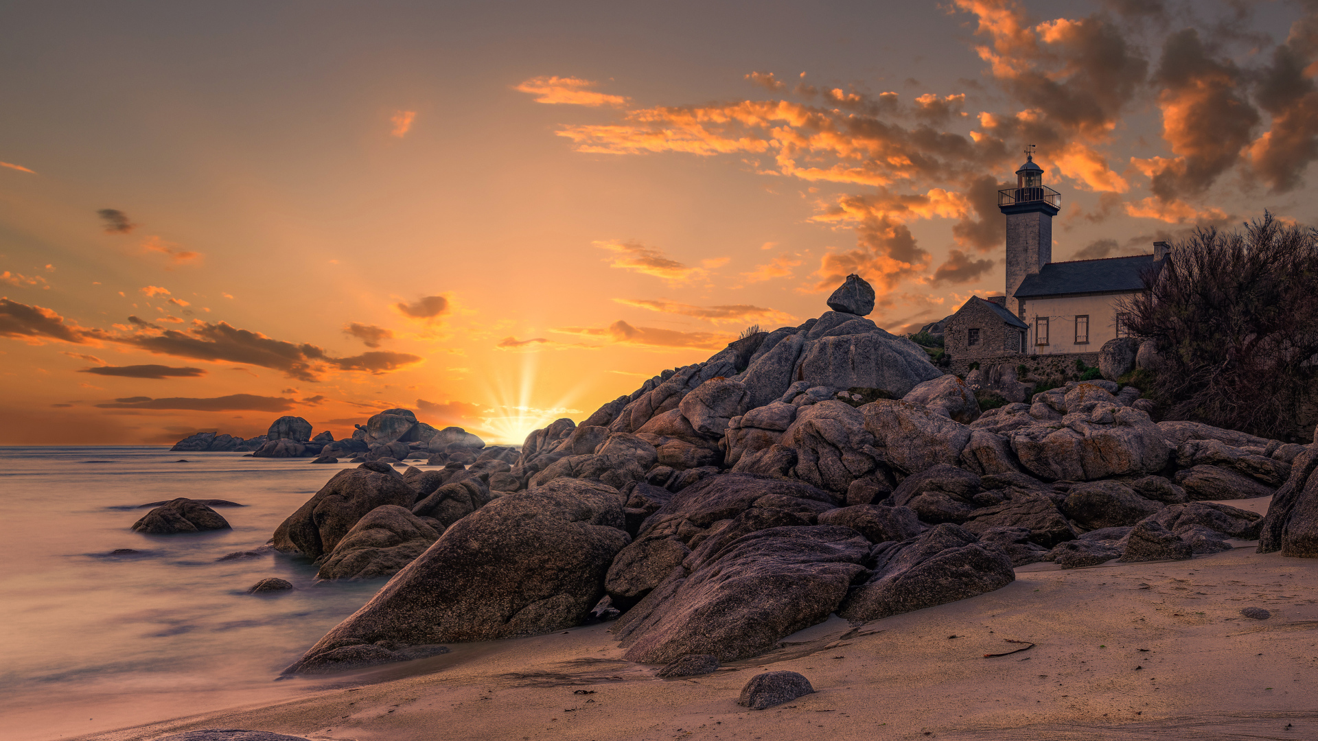 Lighthouse on the shore of a stone shore at sunset