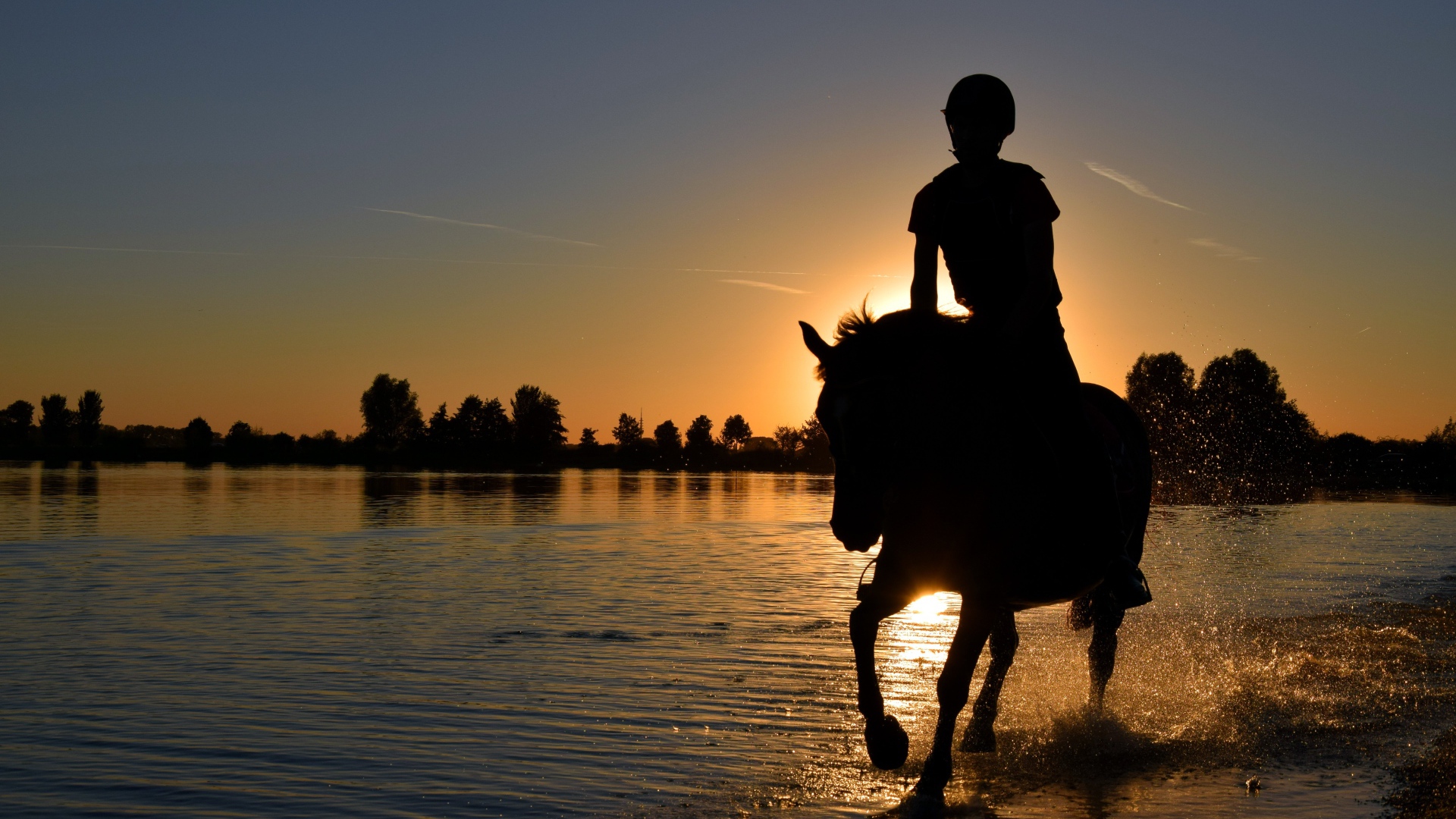 Девушка на лошади скачет по воде на фоне заката