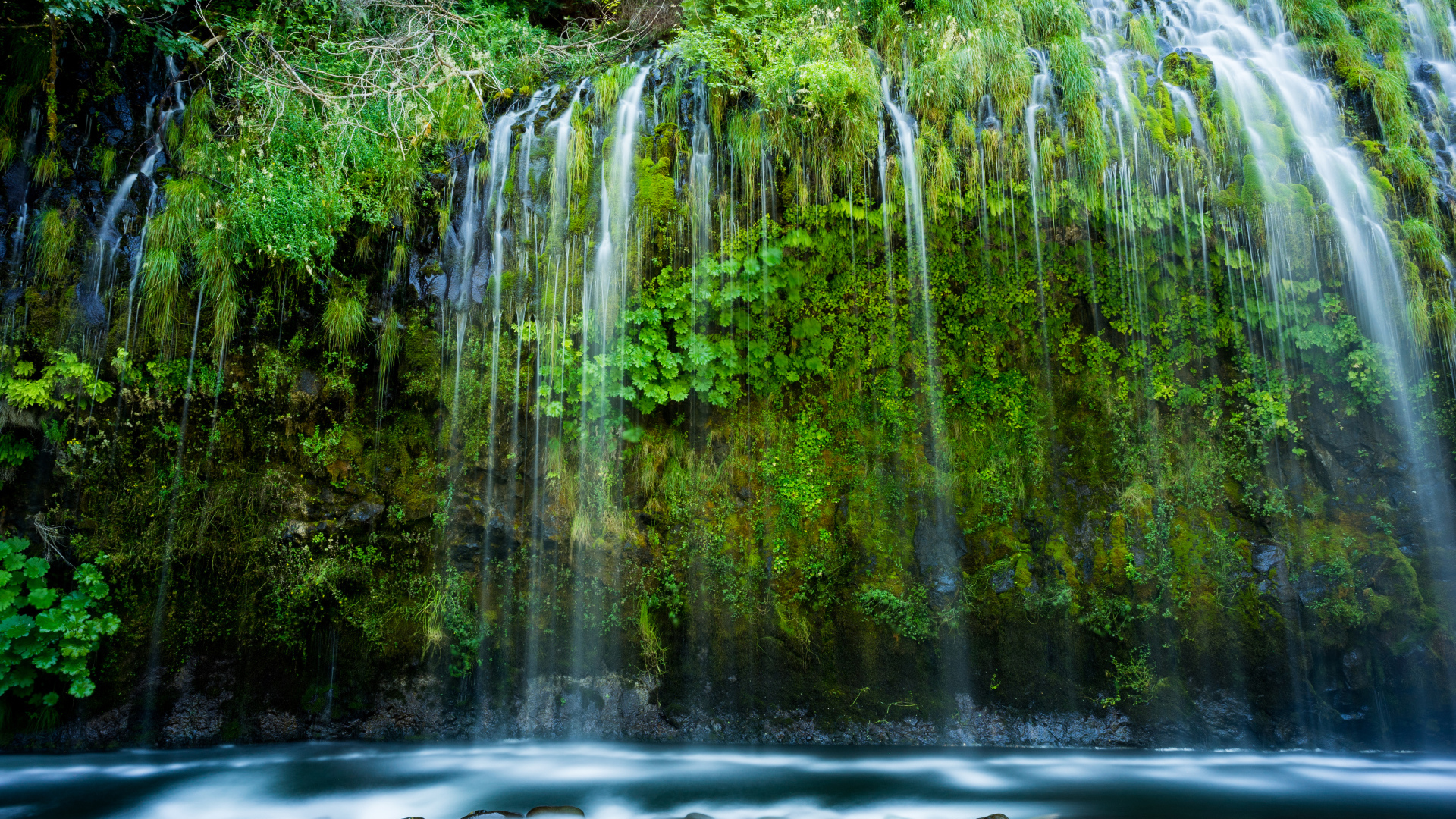 Красивый водопад стекает по покрытом зеленью утесе 