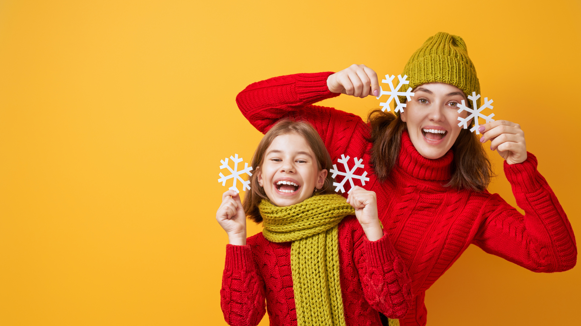 Веселые мама и дочка в красных свитерах на оранжевом фоне