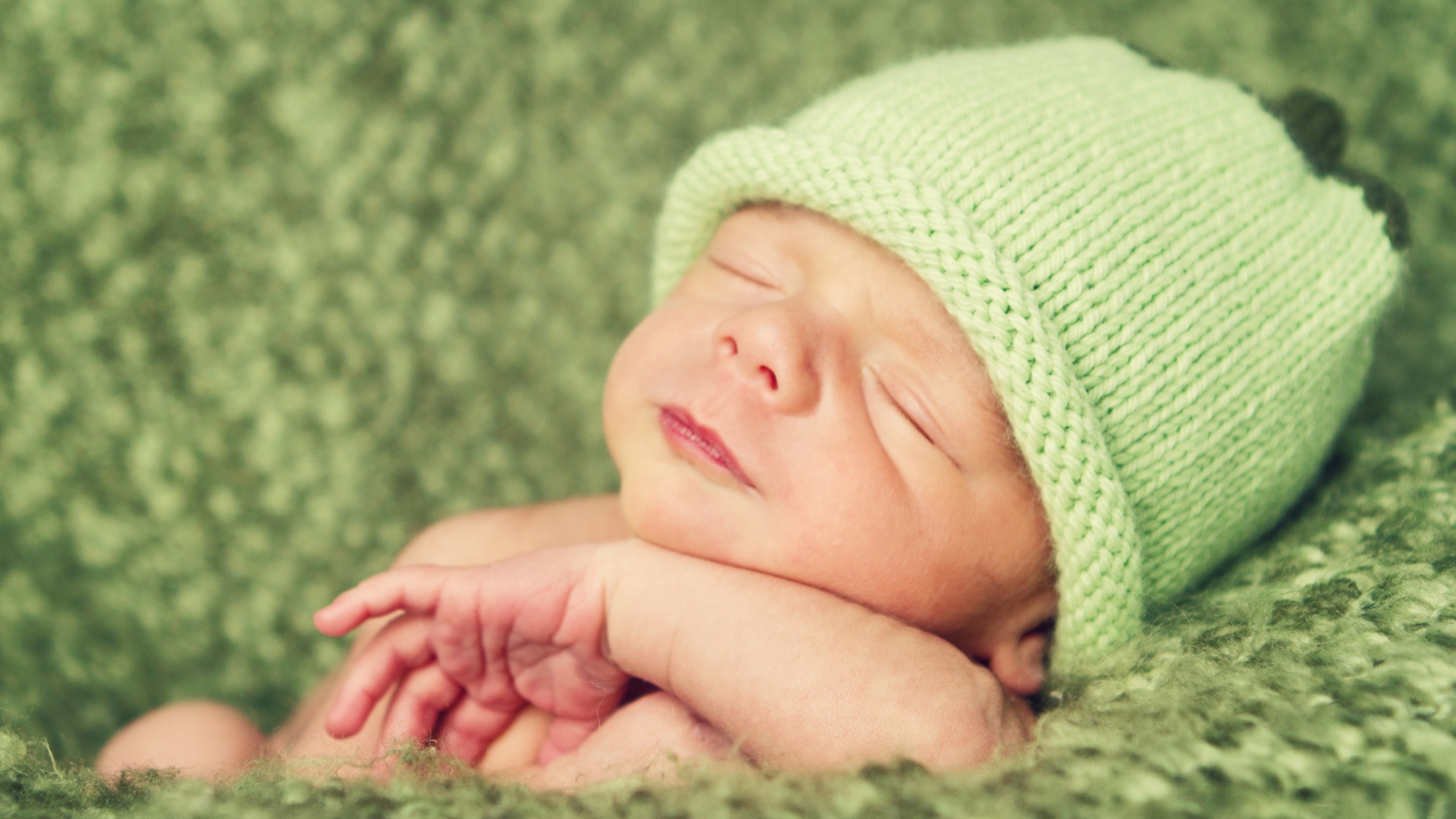 Зеленая вязаная шапка на голове у спящего ребенка 