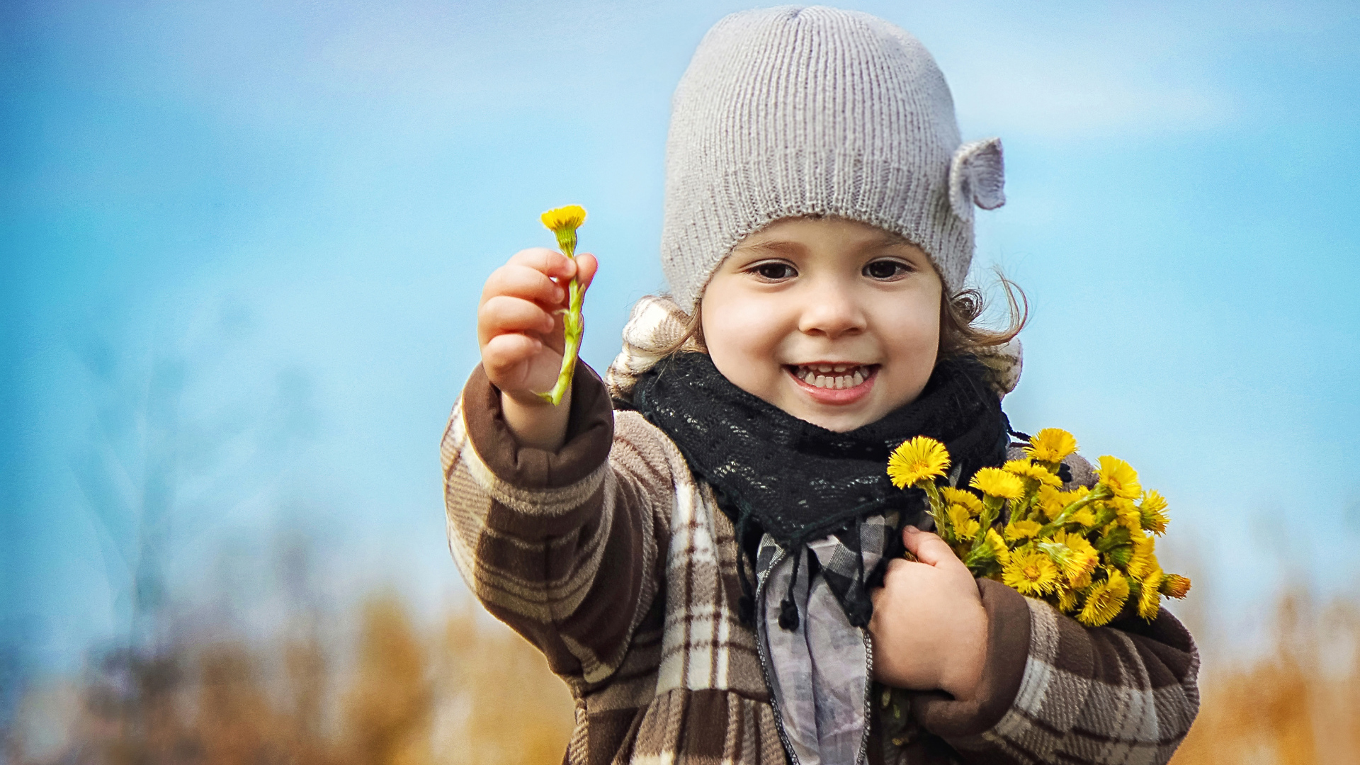 Маленькая девочка в шапке с желтыми цветами в руке