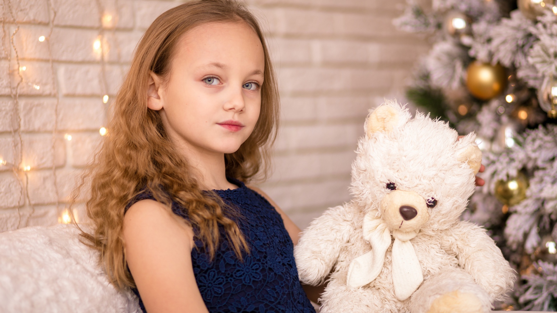 Маленькая девочка с мишкой сидит у наряженной ели 