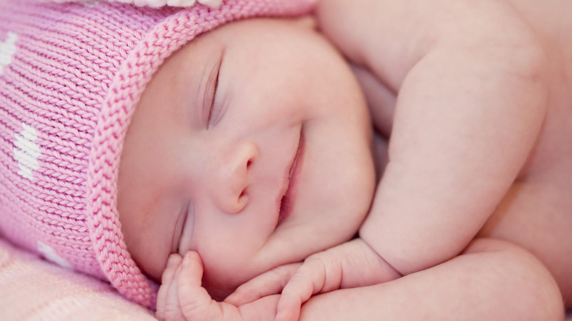 Улыбающийся грудной ребенок в розовой вязаной шапке 