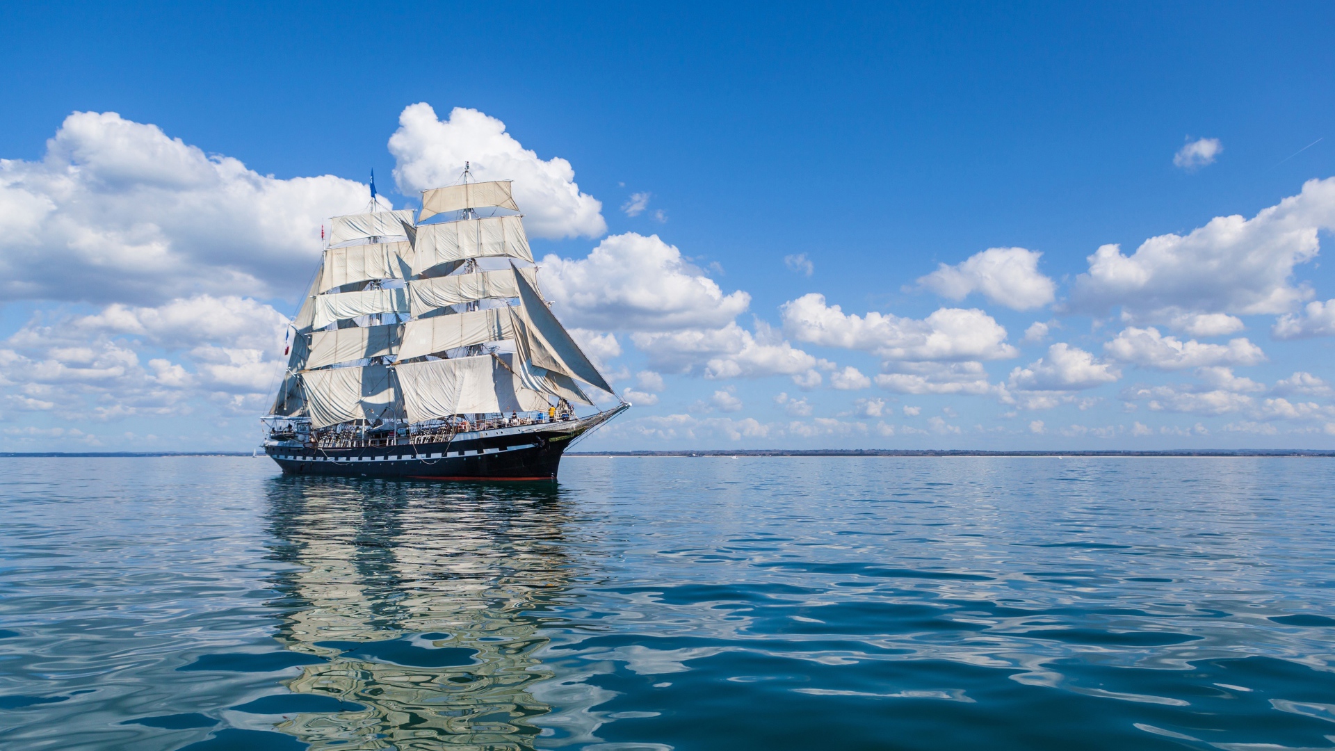 Big ship with white sails at sea under blue sky