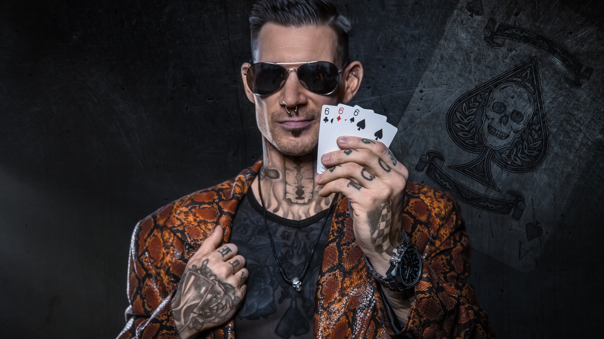 Мужчина с татуировками на теле держит в руке три карты шестерки 