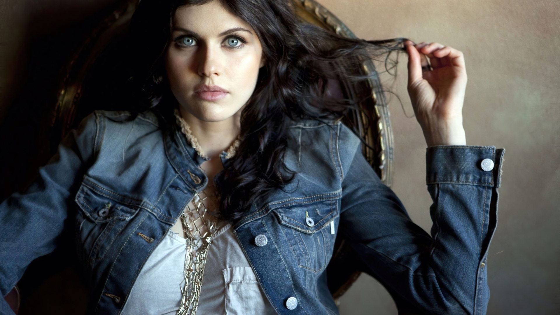 Actress Alexandra Daddario in a denim jacket sits in a chair