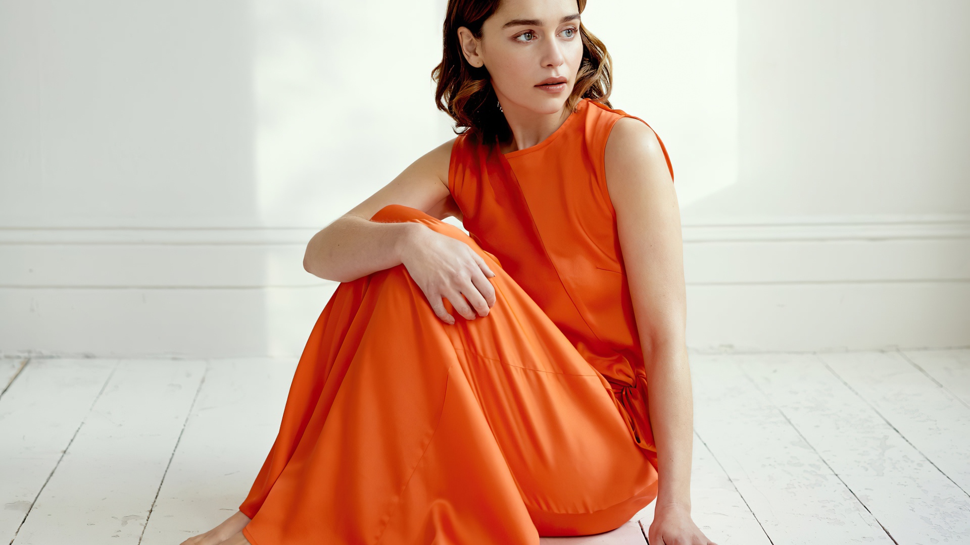 Актриса Эмилия Кларк  в оранжевом платье сидит на полу