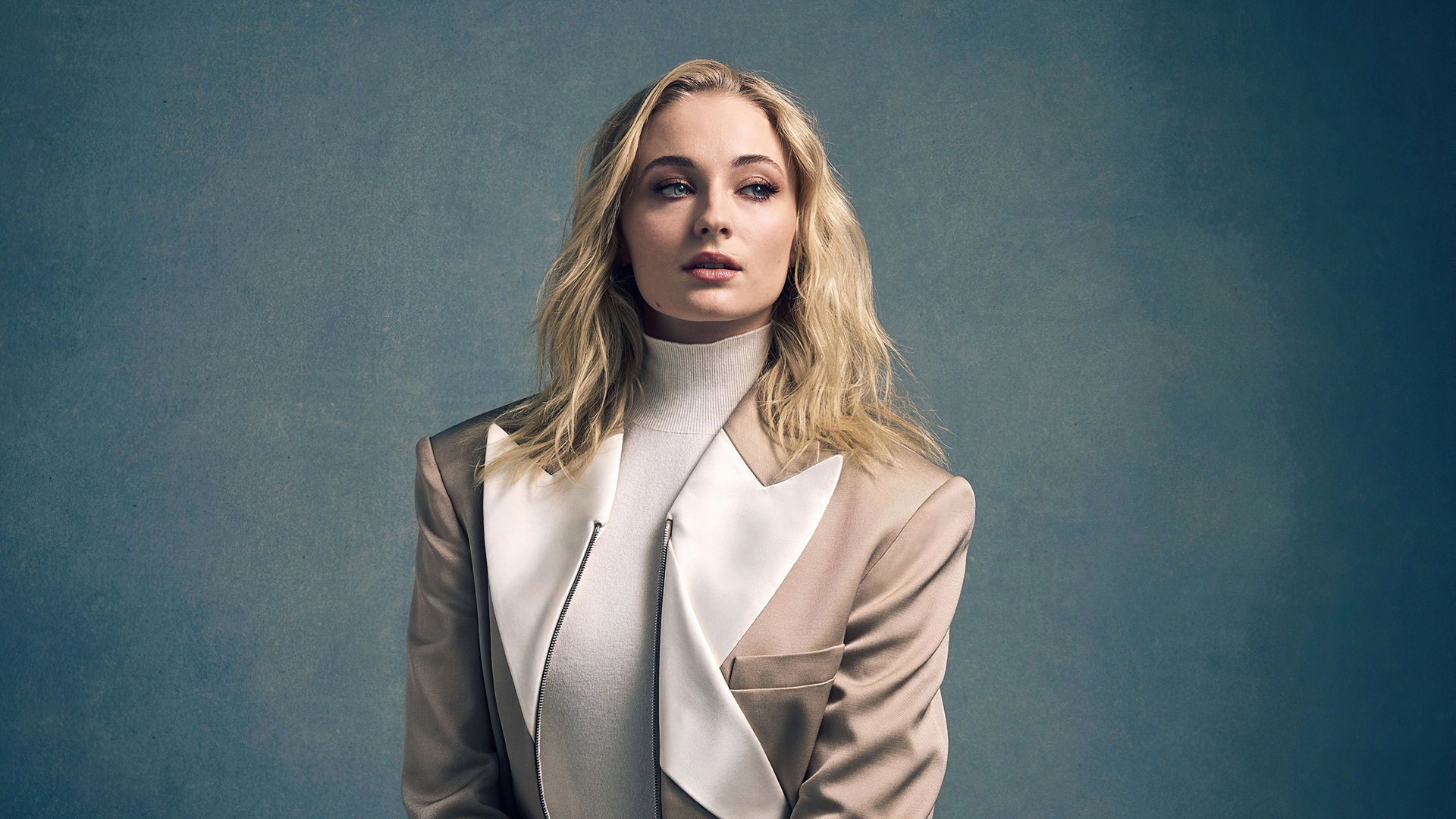 Актриса Софи Тёрнер в бежевом костюме на сером фоне