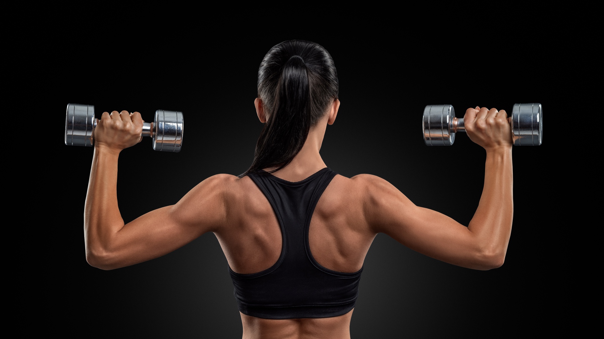 Стройная спортивная девушка с гантелями в руках на черном фоне