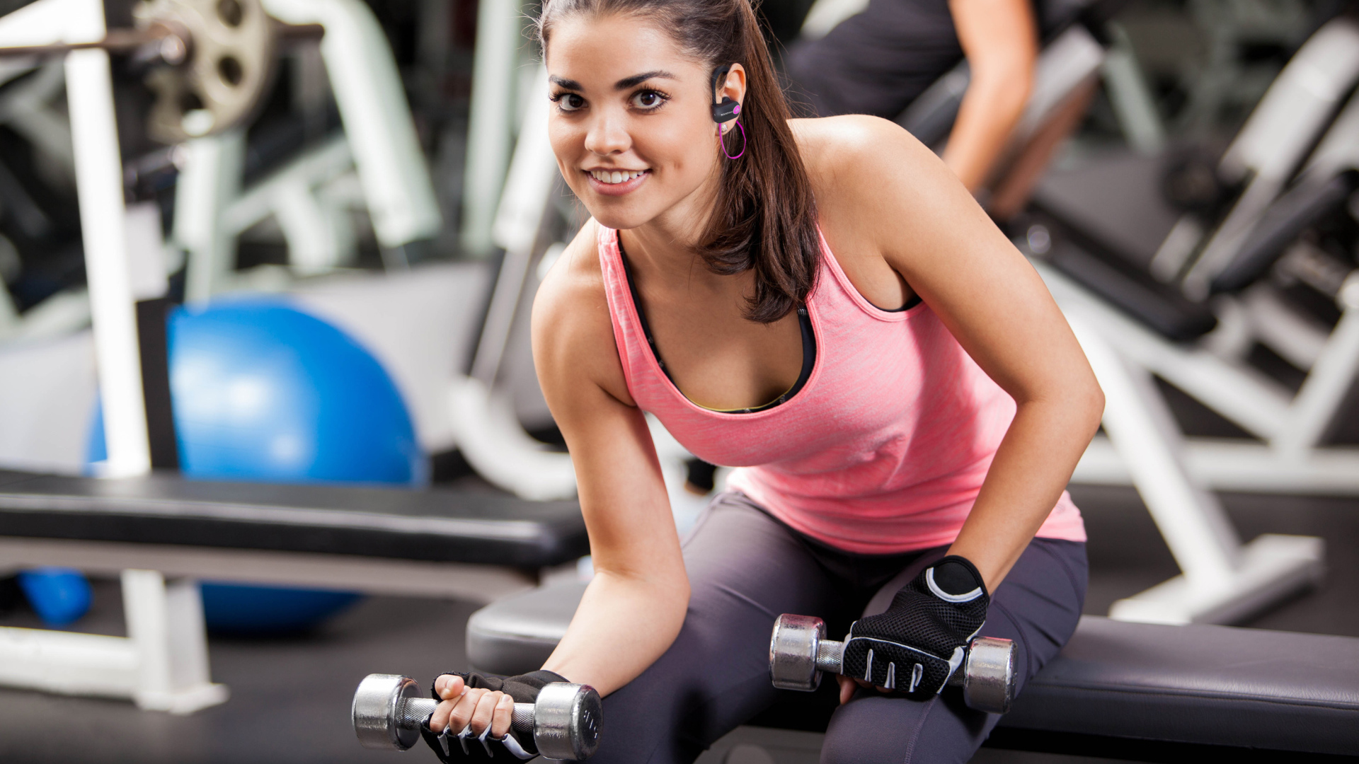Улыбающаяся девушка качается гантелями в спортзале