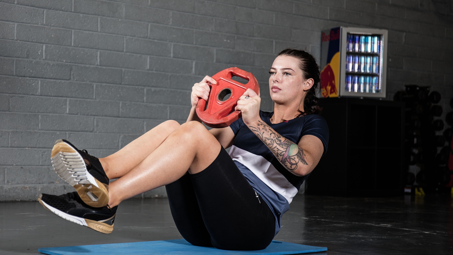 Сильная девушка с татуировками на руке качает пресс 