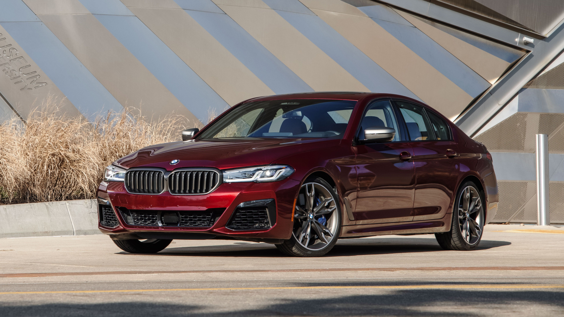 Бордовый седан BMW M550i XDrive, 2021 года у здания