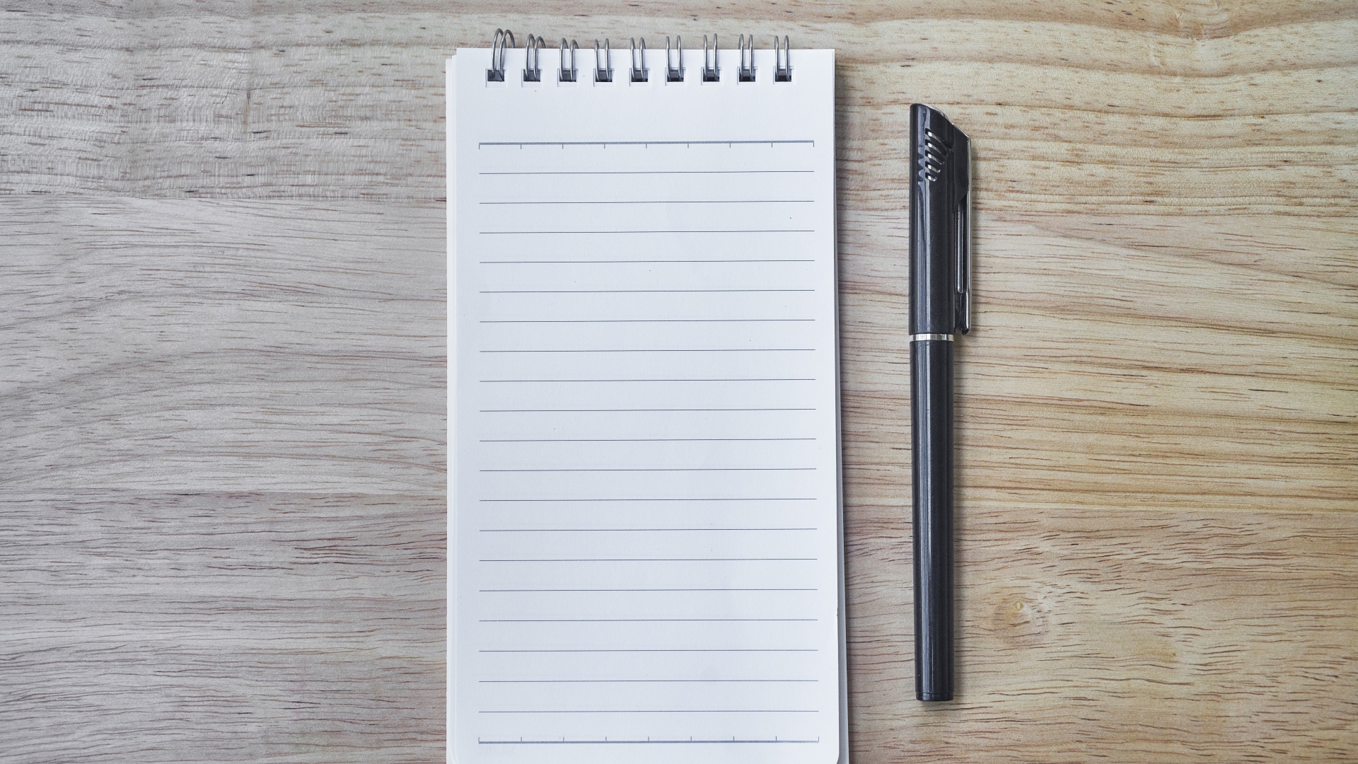 Авторучка и блокнот лежат на деревянном столе