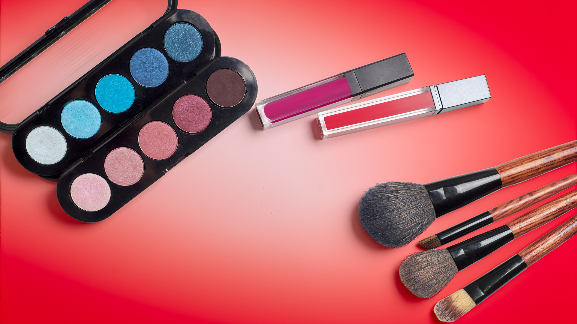 Блеск для губ, тени и кисточки на красном фоне