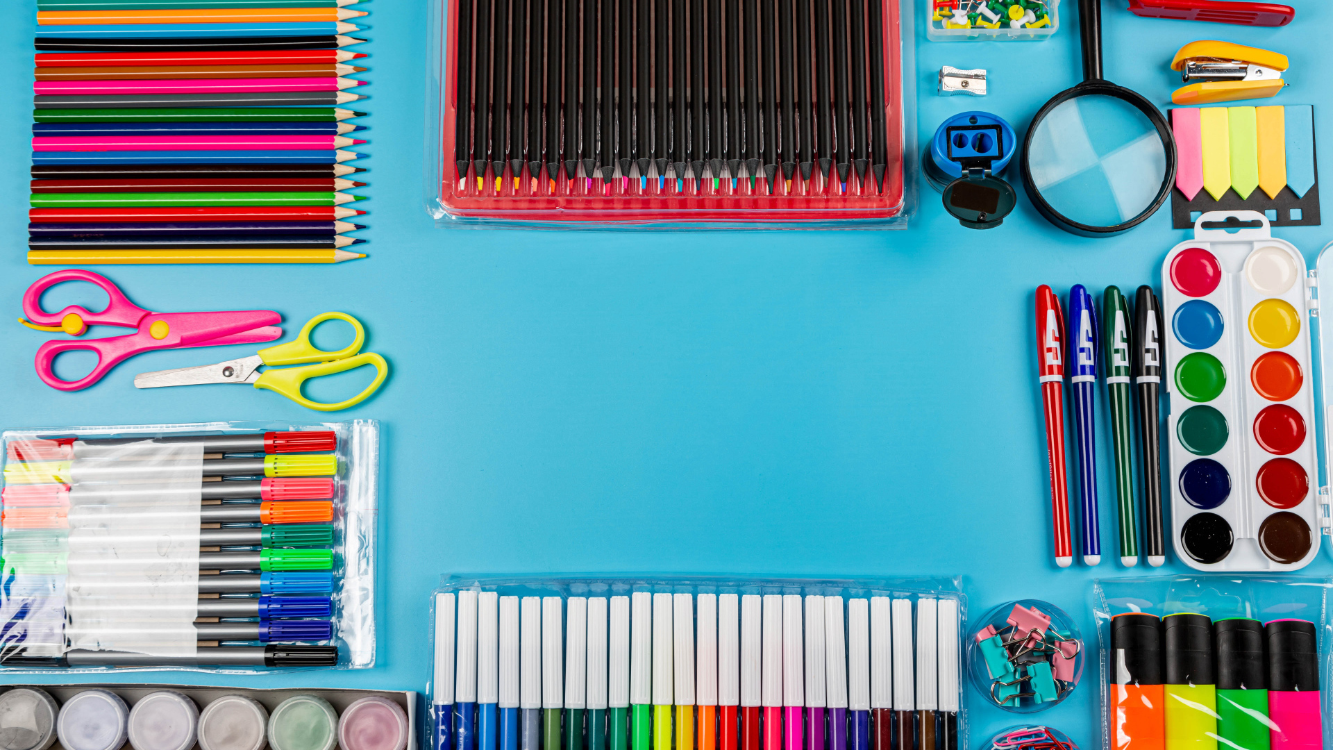 Много разноцветных канцелярских предметов на голубом фоне 