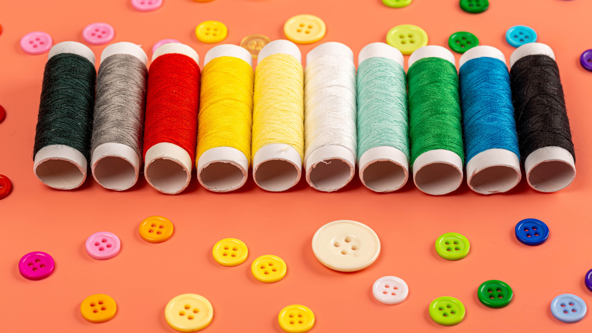 Разноцветные нитки и пуговицы на розовом фоне
