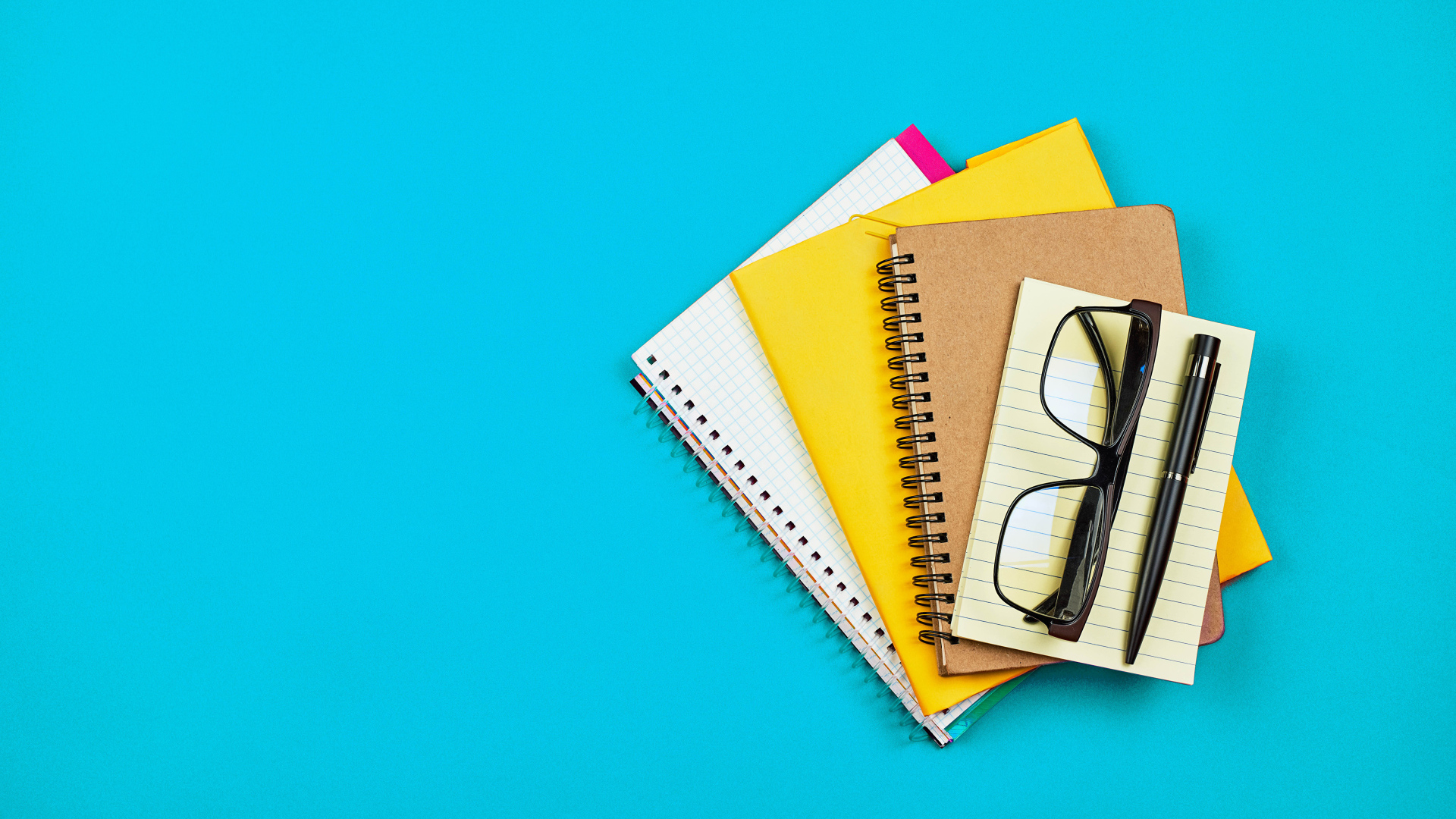 Блокноты, очки и ручка на голубом фоне