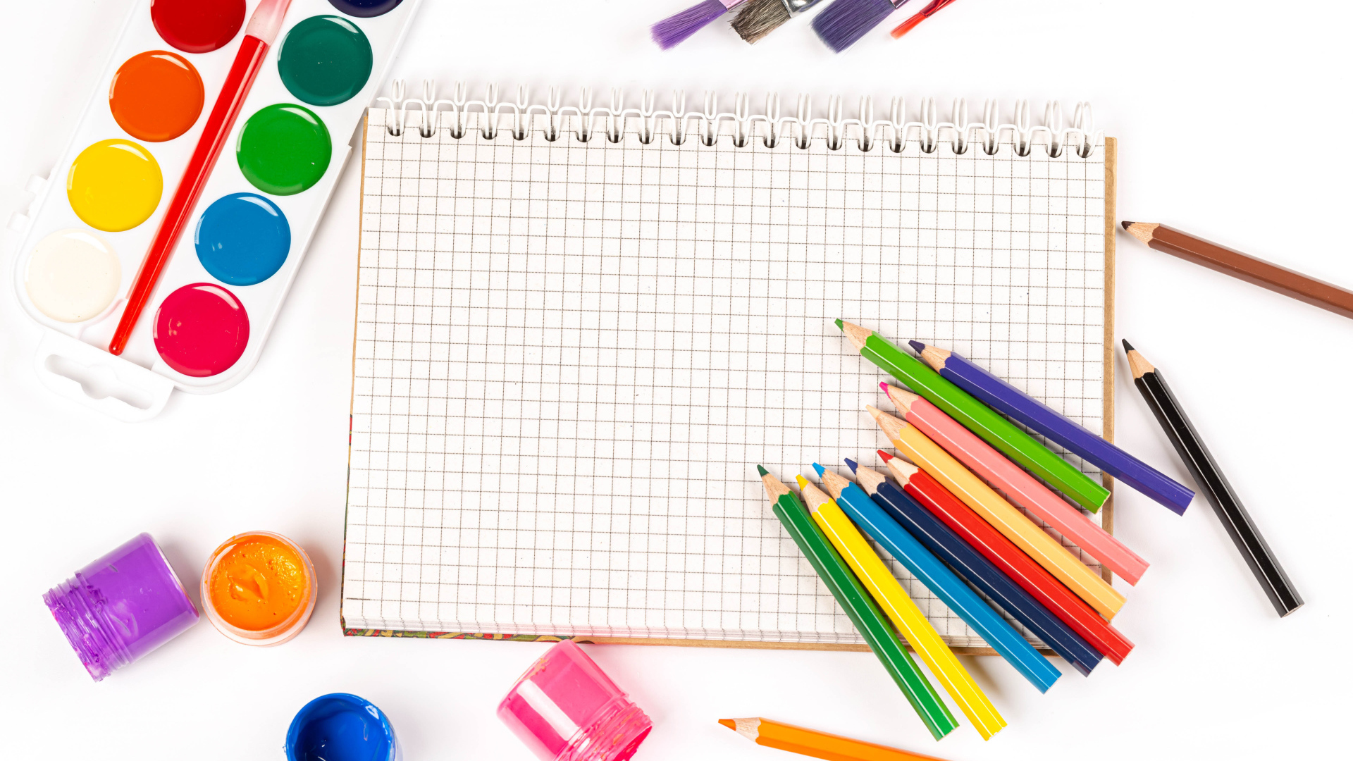 Карандаши, краски и тетрадь на белом фоне 