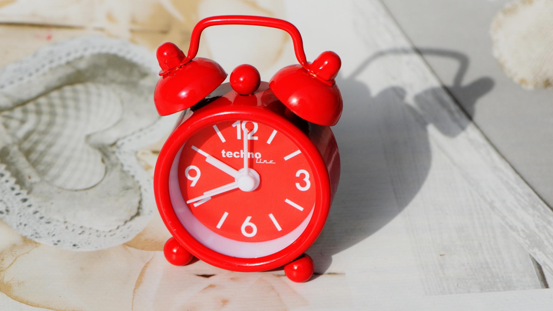 Маленький красный будильник стоит на столе 