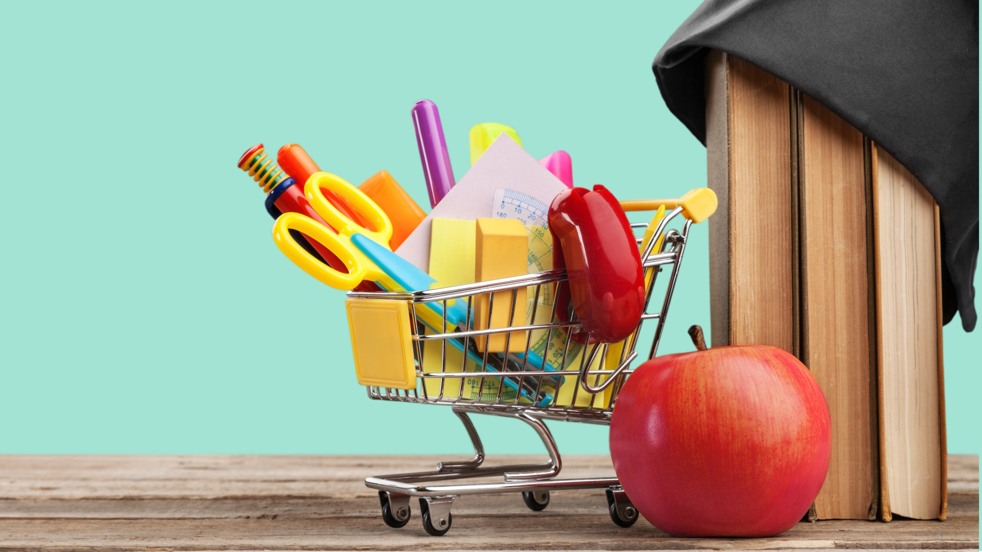 Канцелярские предметы в тележке на столе с яблоком и книгами 