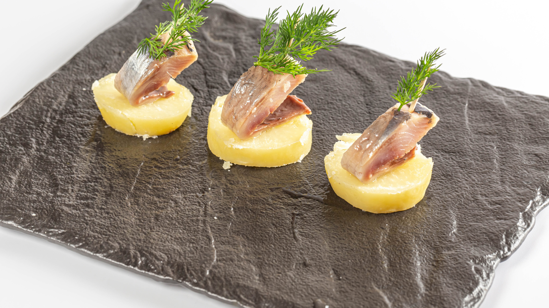 Три куска вареного картофеля с сельдью и укропом