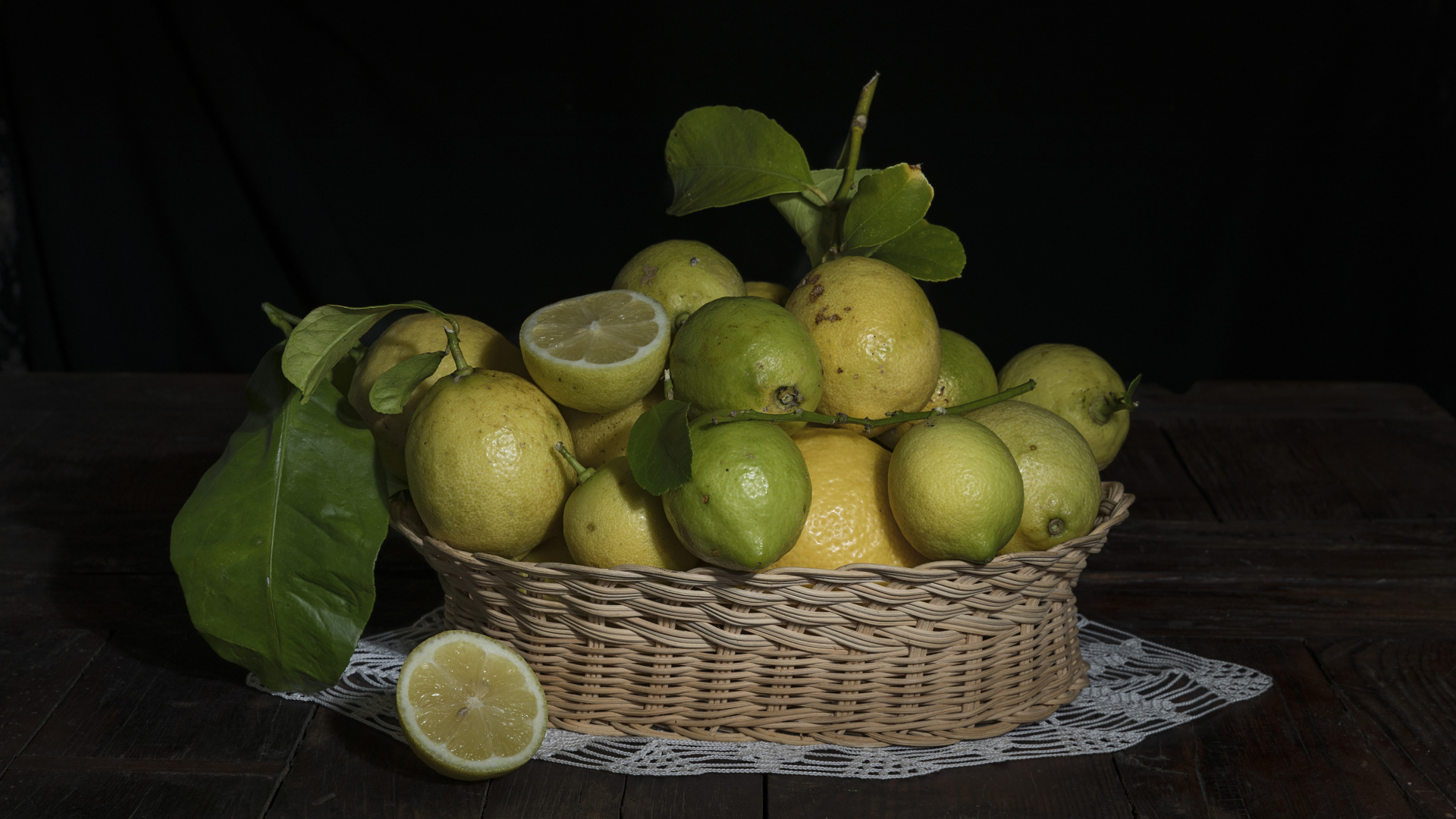 Лимоны и лаймы в плетеной корзинке на черном фоне