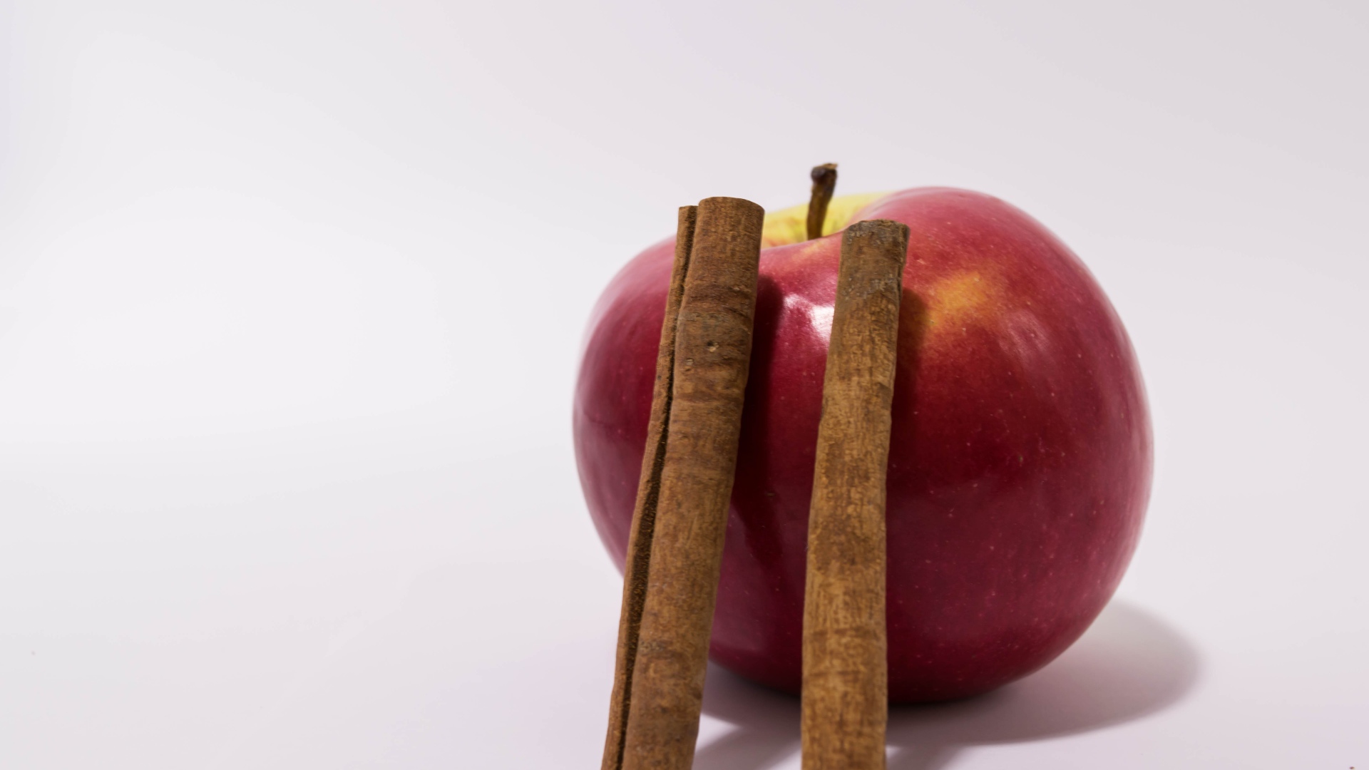 Красное яблоко с палочками корицы на сером фоне