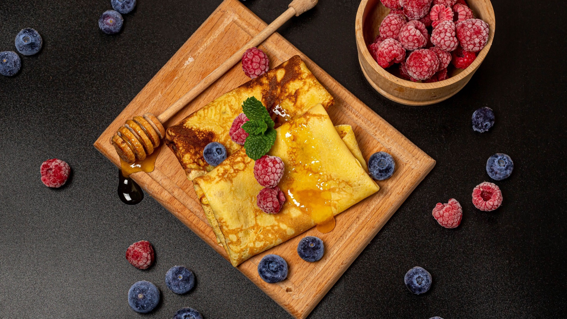 Блины с медом и ягодами черники и малины на черном столе 