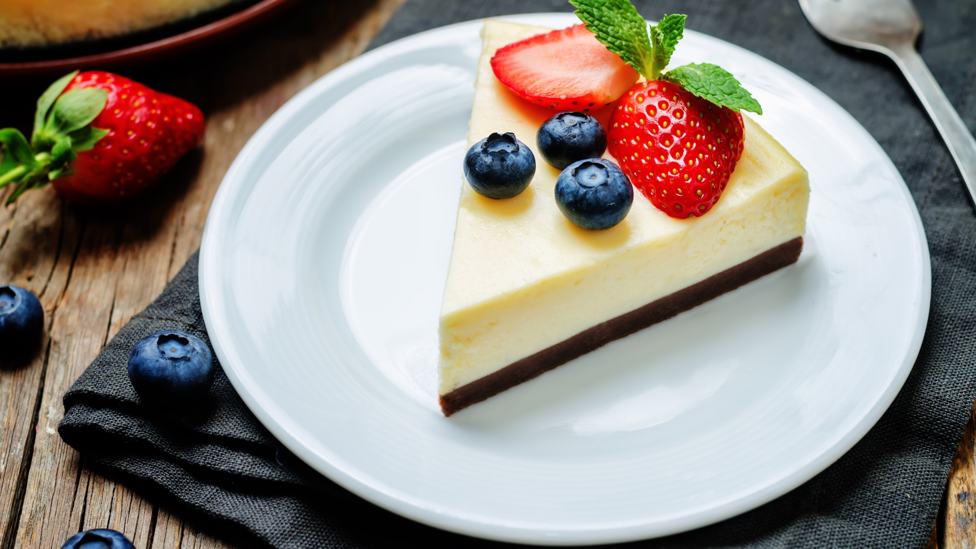 Кусок чизкейка на белой тарелке с клубникой и черникой 