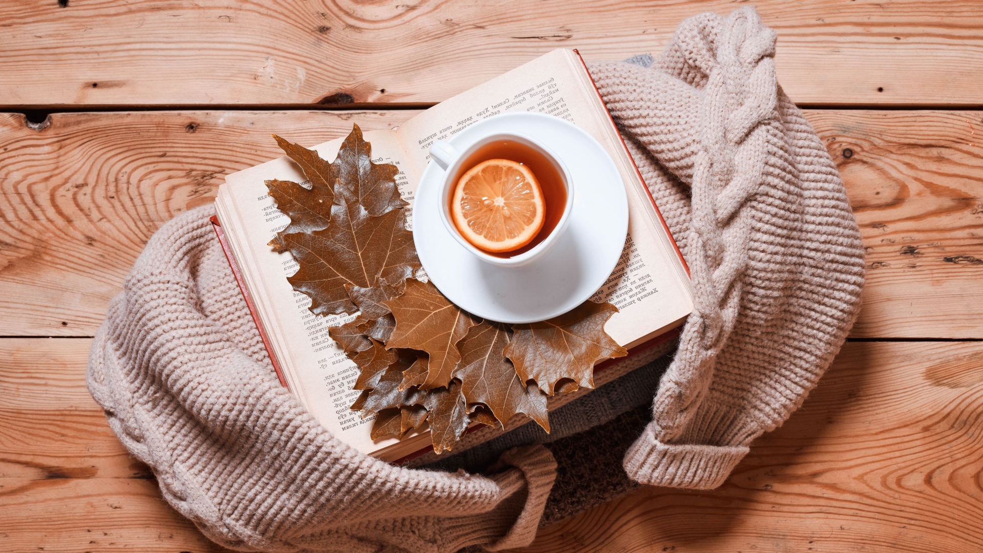 Чашка чая с лимоном на столе с книгой и теплой кофтой