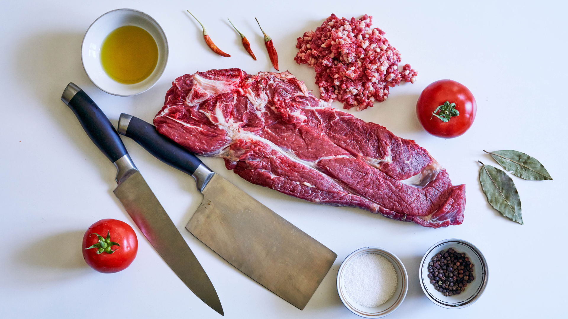 Кусок мяса со специями и ножами на столе 