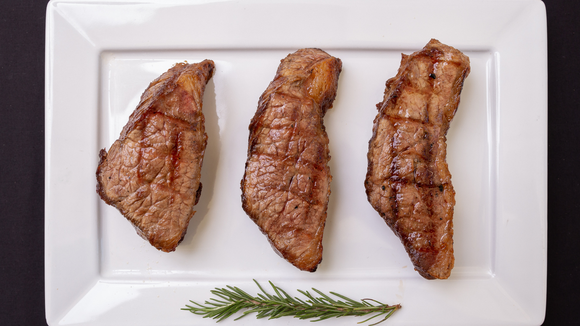 Three pieces of grilled meat on a large white plate