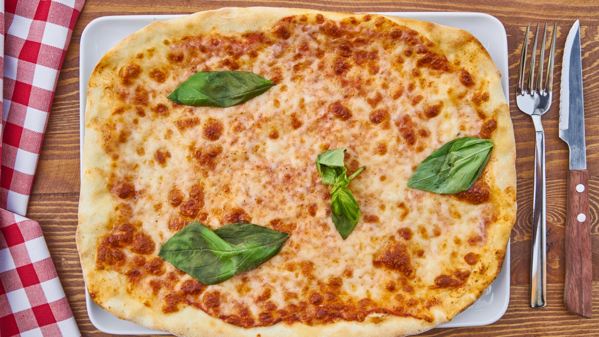 Пицца с сыром и листьями базилика на столе со столовыми приборами