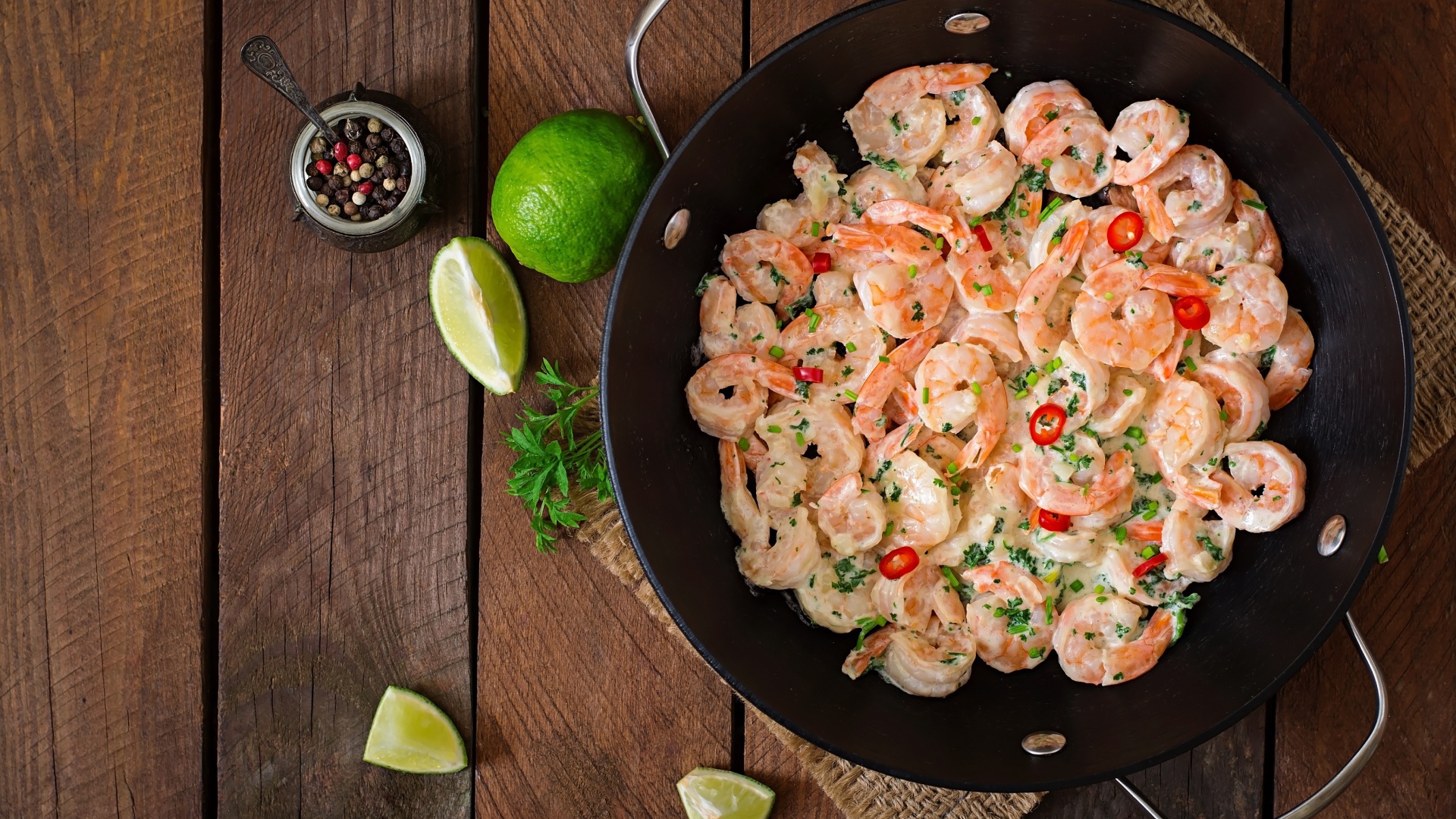 Креветки с соусом в сковороде на столе с лаймом