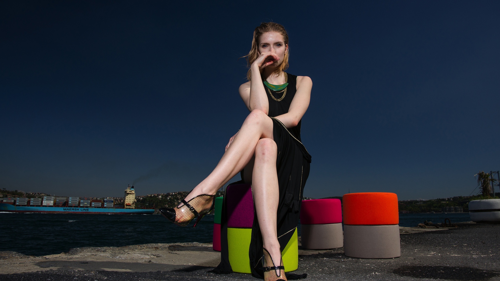 Девушка в черном платье сидит у воды