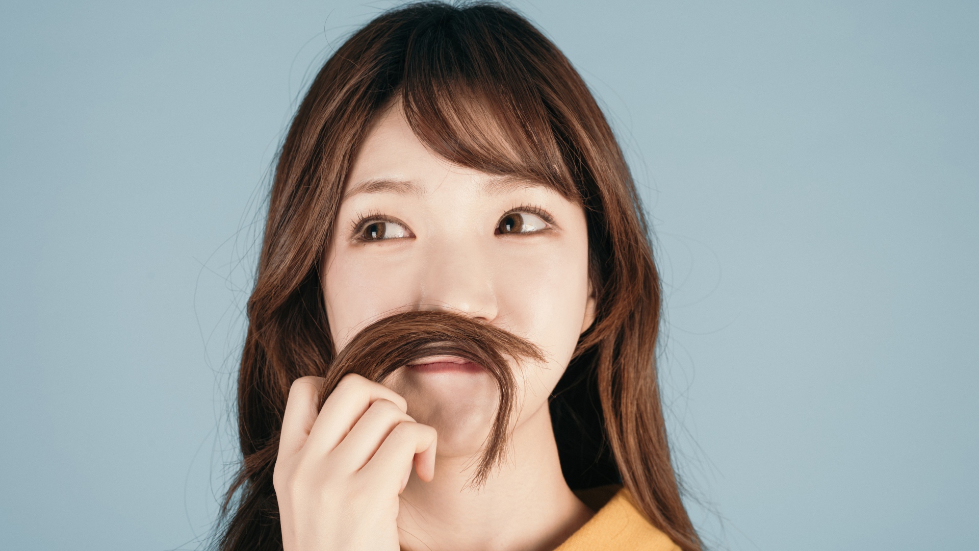 Девушка азиатка закрыла лицо волосами на сером фоне 