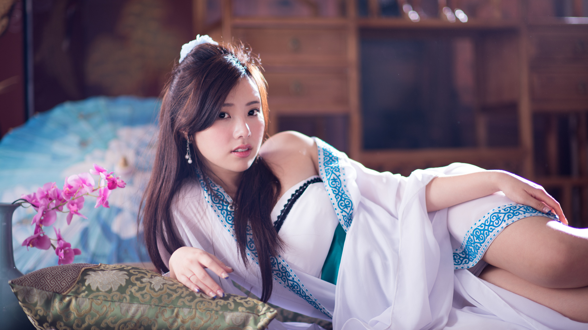 Девушка азиатка в красивом платье лежит на кровати 