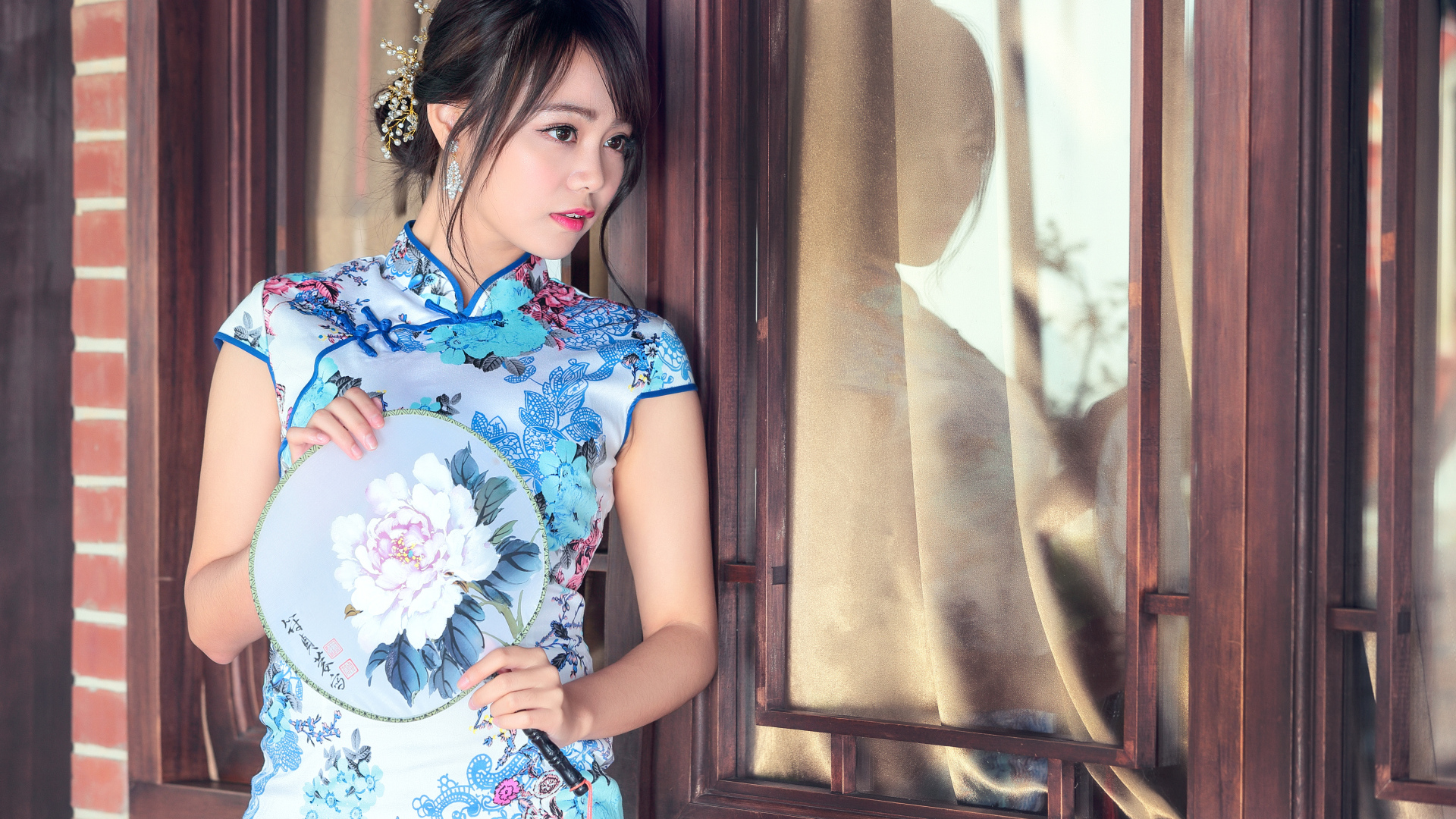 Девушка азиатка в красивом платье стоит у окна 