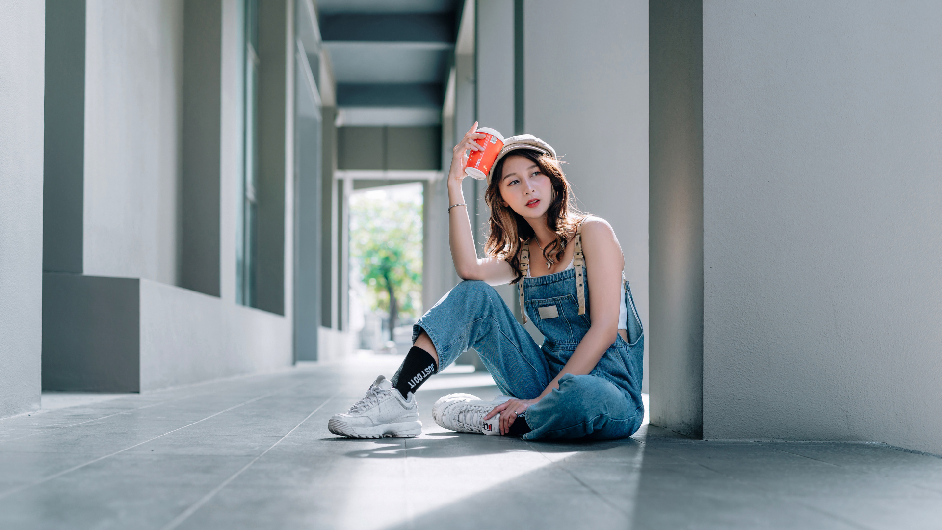 Девушка азиатка в синем комбинезоне с кофе в руке 