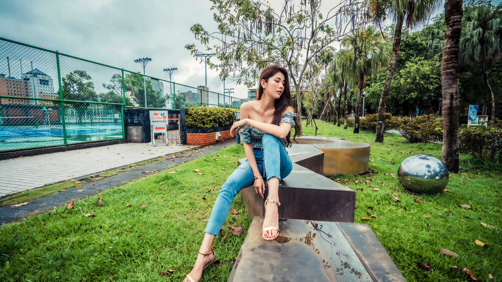 Девушка азиатка в джинсах сидит в парке 