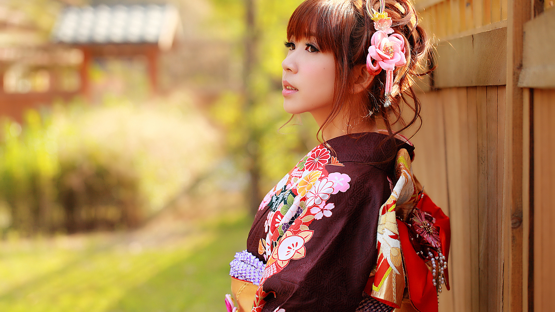 Девушка азиатка в кимоно стоит у забора 
