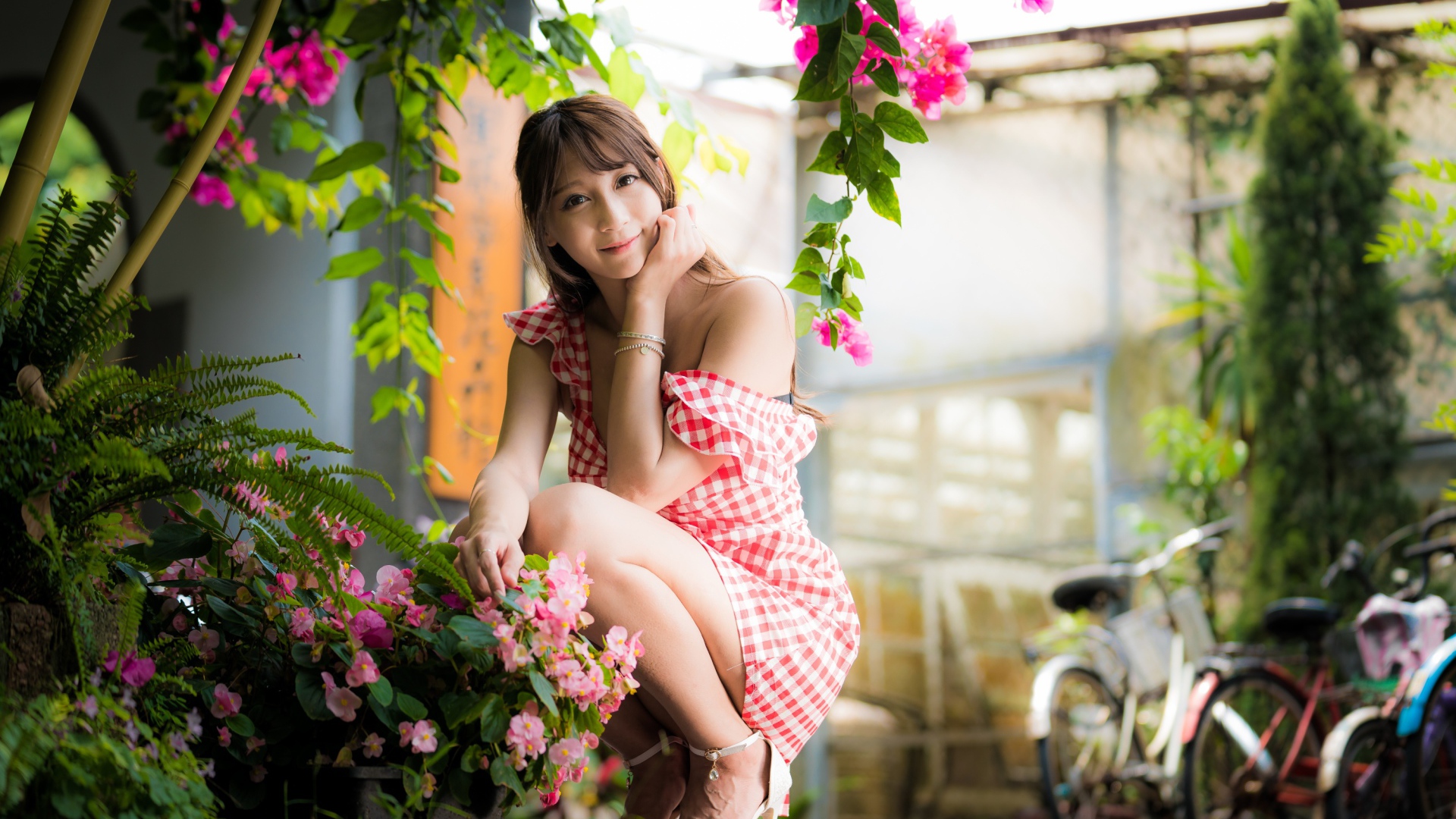 Девушка азиатка сидит на корточках у розового цветка