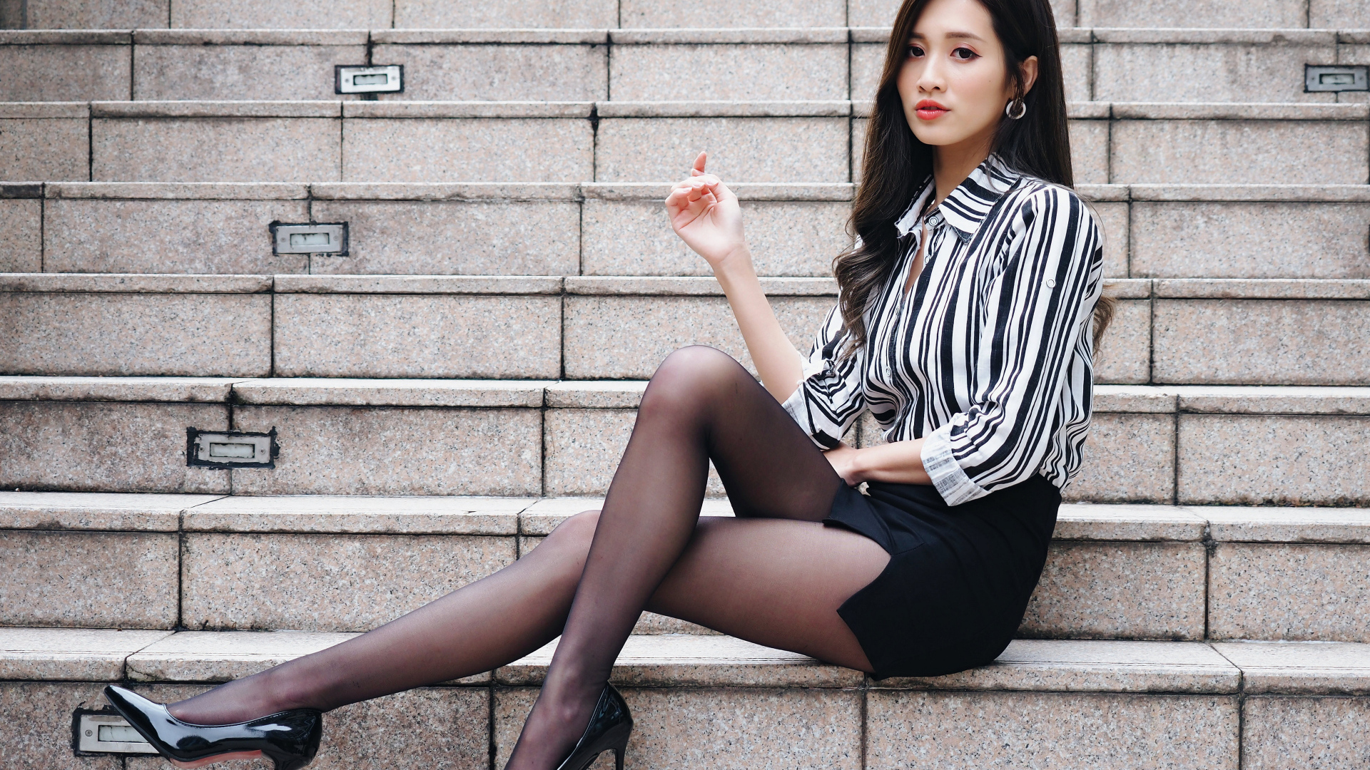 Красивая девушка азиатка в юбке сидит на ступеньках